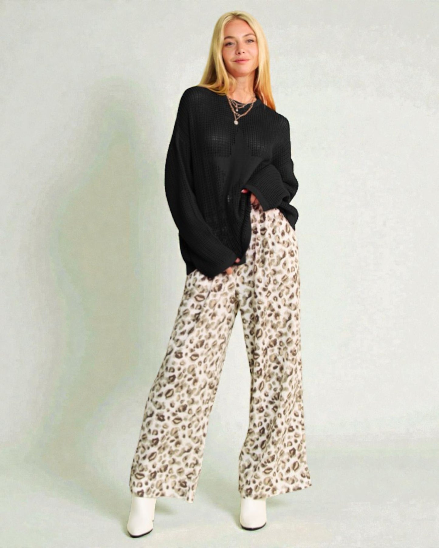 Woman wearing a black sweater and leopard print pants on a light gray background