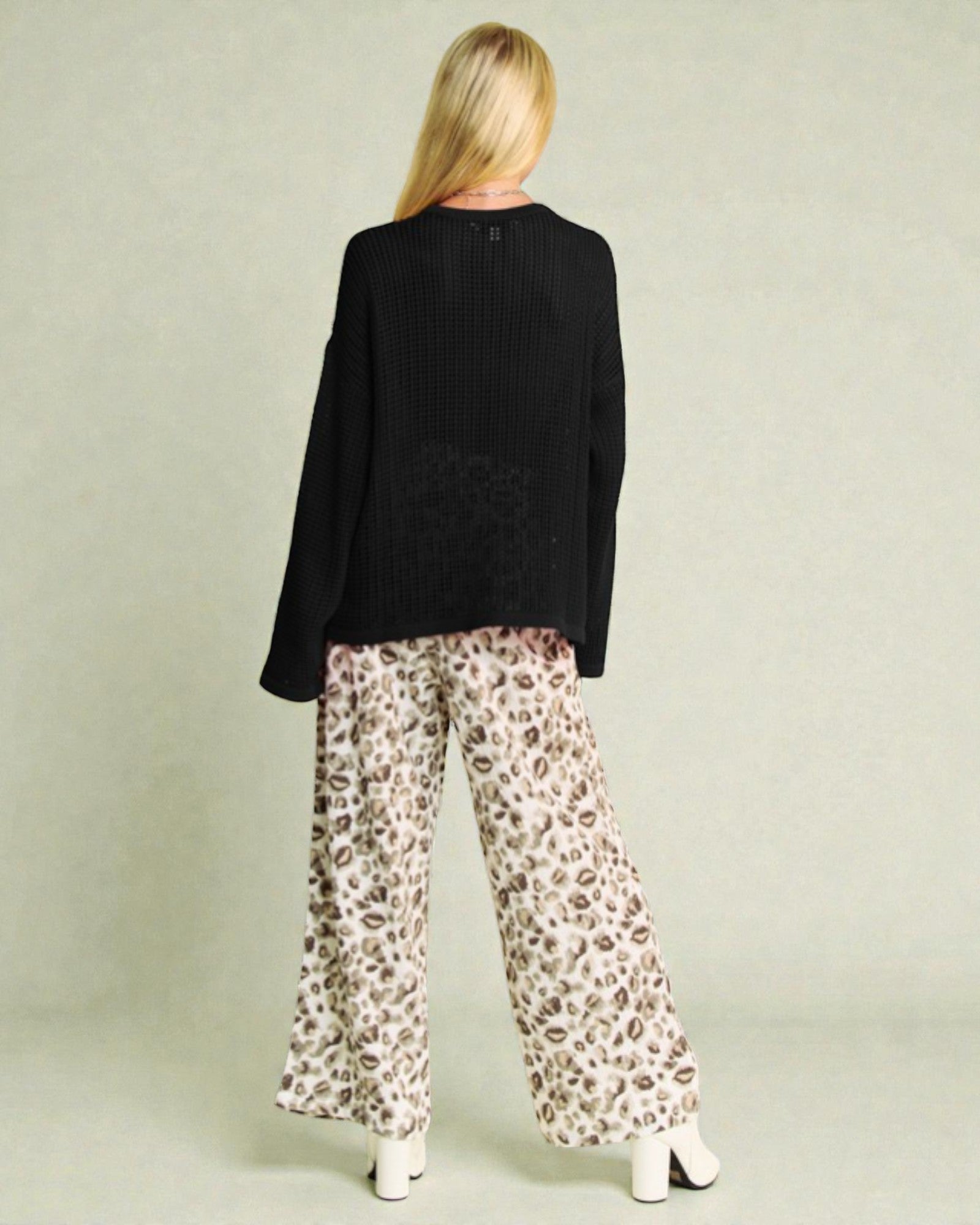 Person wearing a black sweater and leopard print pants on a plain background