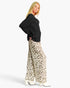 A woman modeling a black ribbed knit sweater and wide-leg leopard-print trousers with white high heels, photographed against a plain light gray studio background.