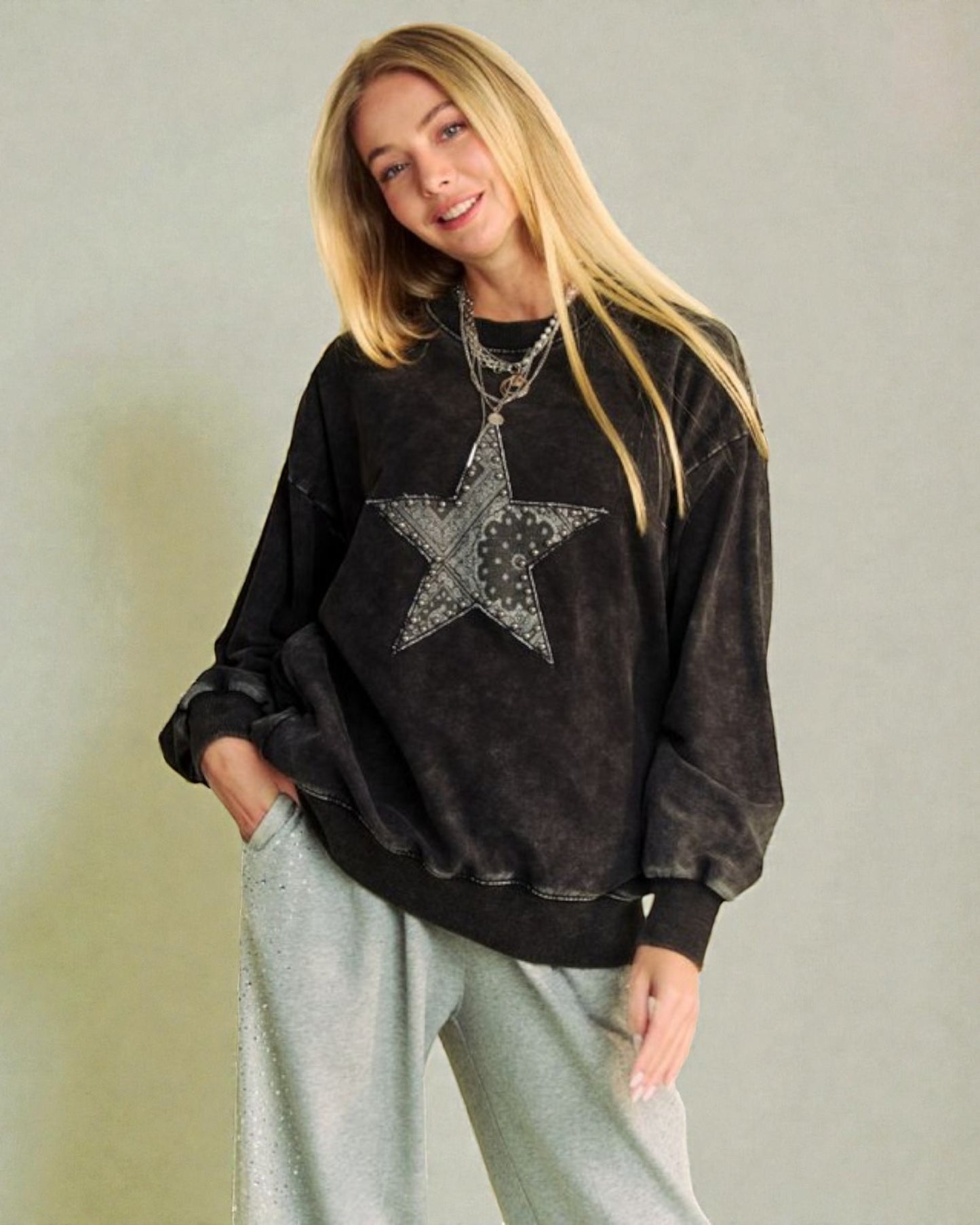 Woman wearing a black sweatshirt with a star design on a plain background