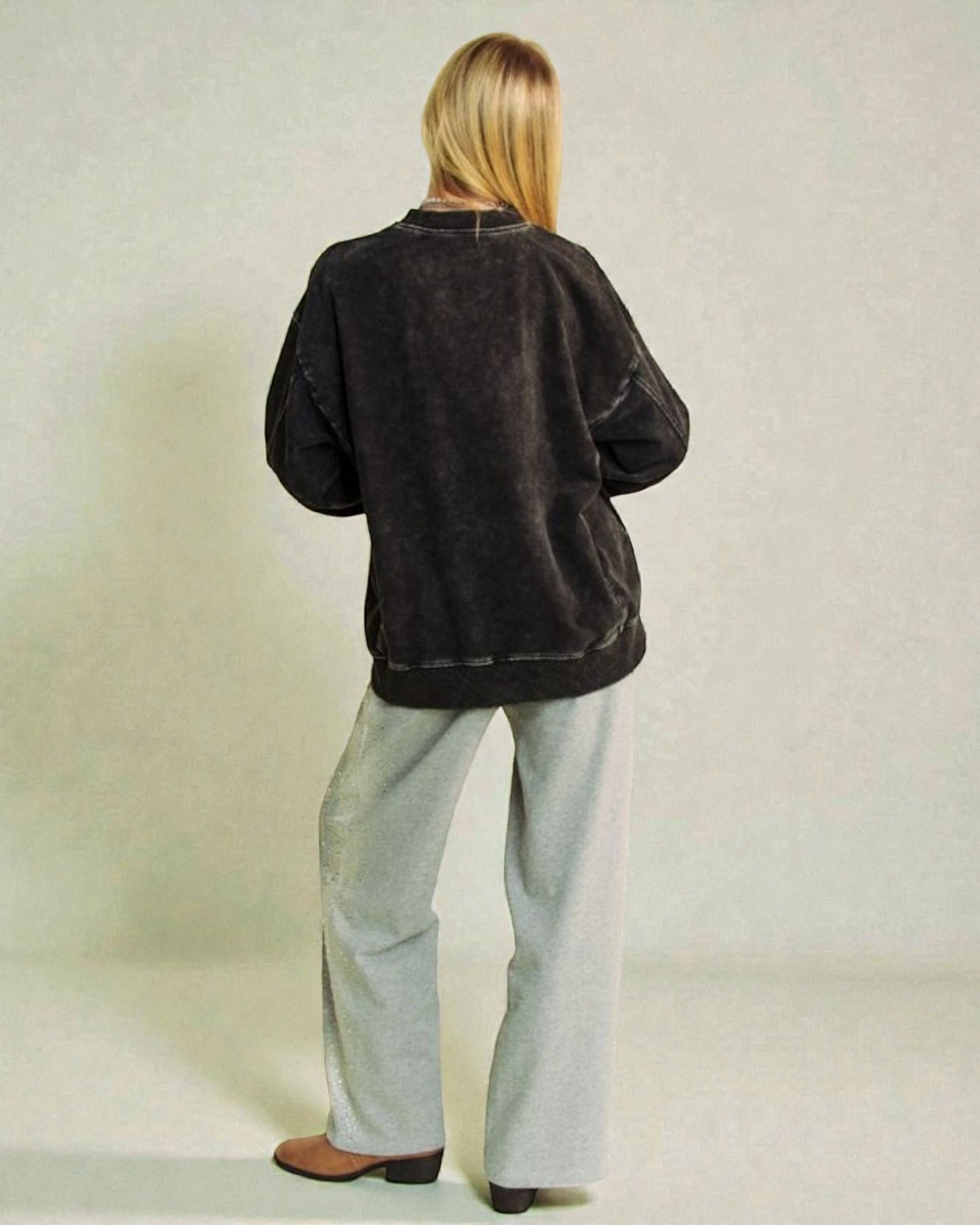 Person wearing a black jacket and light gray pants against a plain background