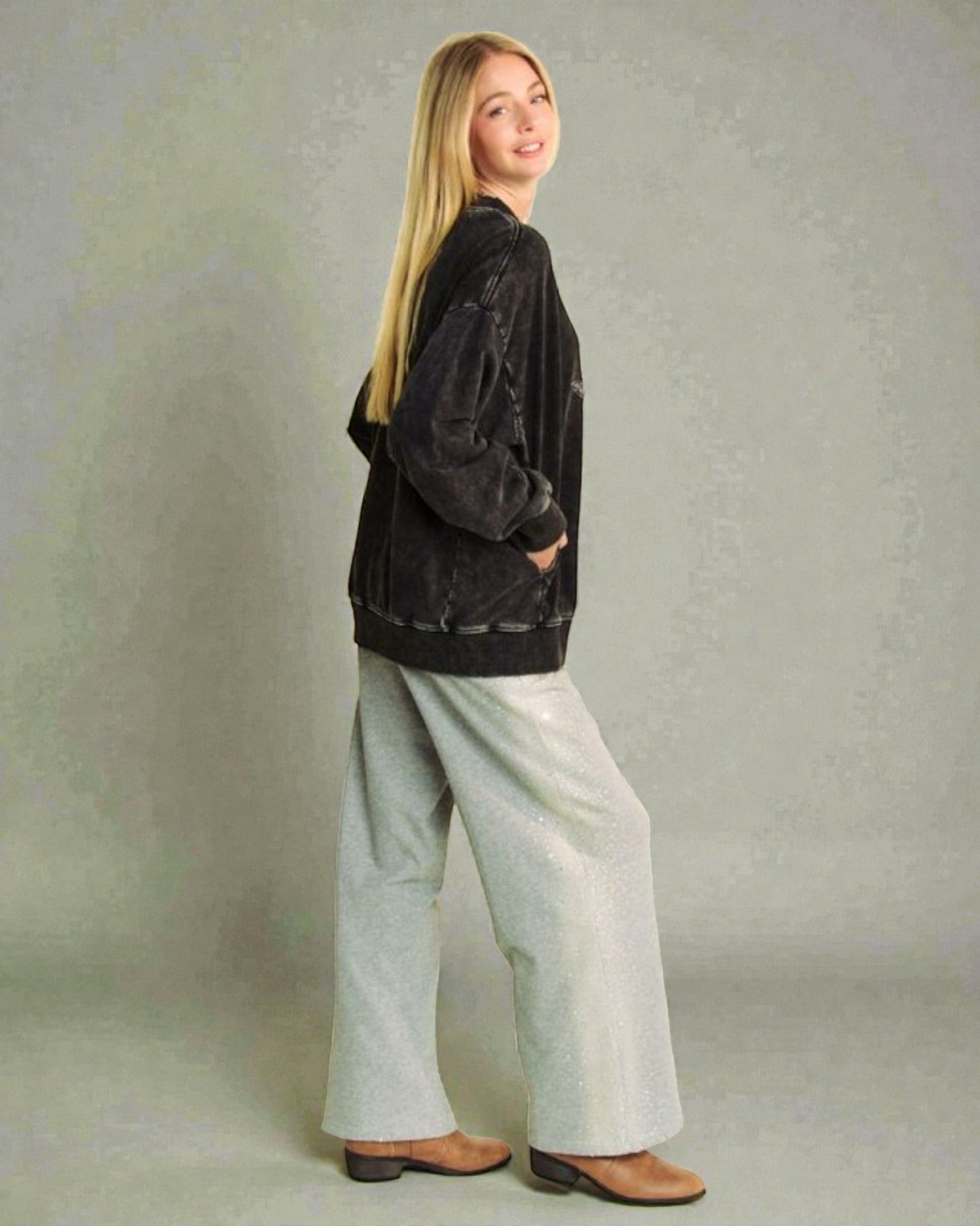 Woman wearing a black jacket and light-colored pants against a plain background