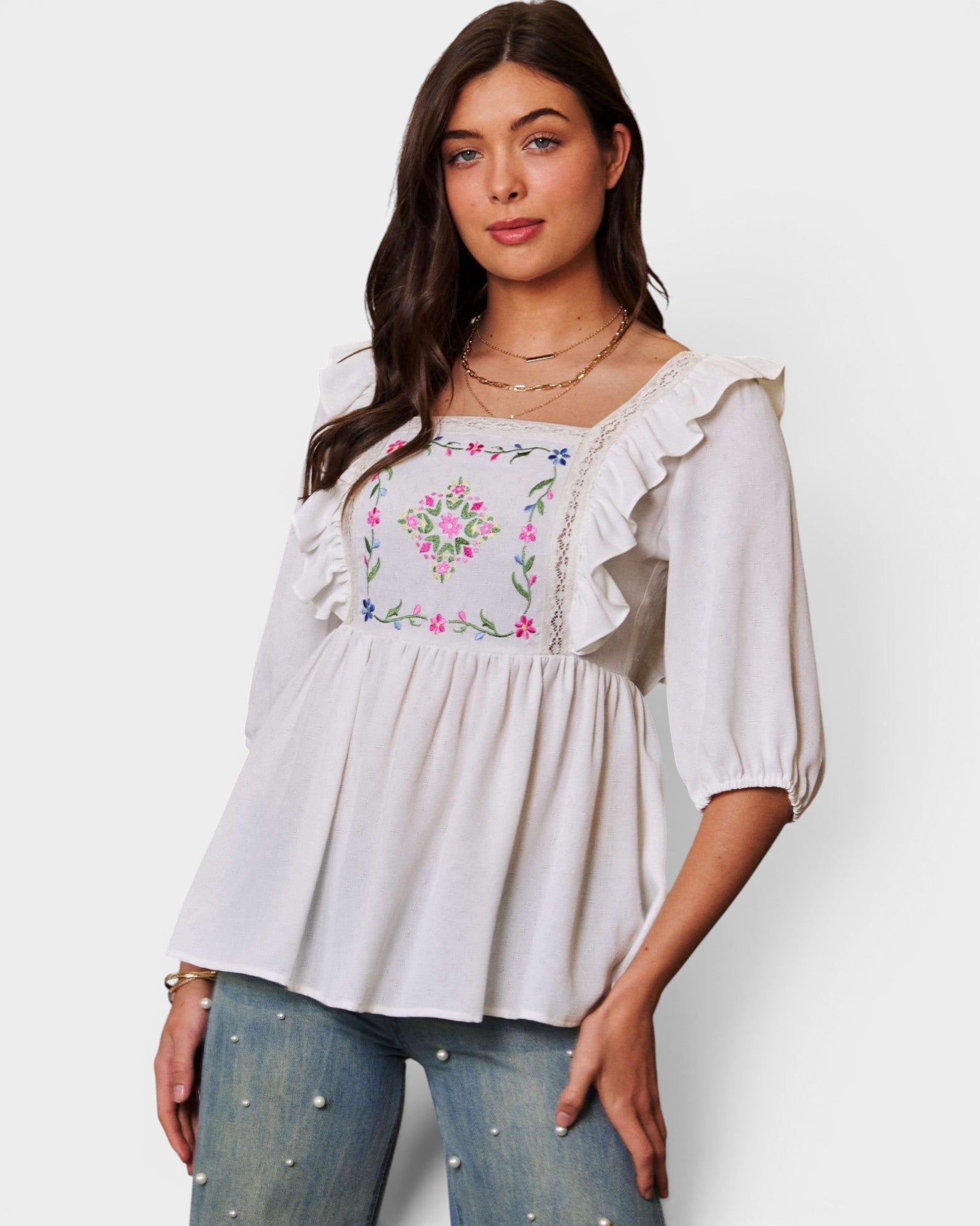 Woman wearing a white blouse with floral embroidery and blue jeans on a white background