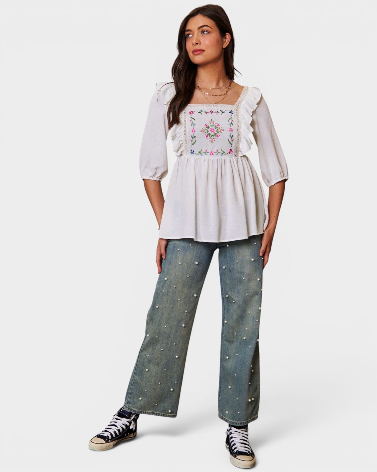 Woman wearing a white blouse with floral embroidery and blue jeans on a white background