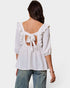 White blouse with ruffled sleeves and open back tied with a bow, worn by a person on a white background.