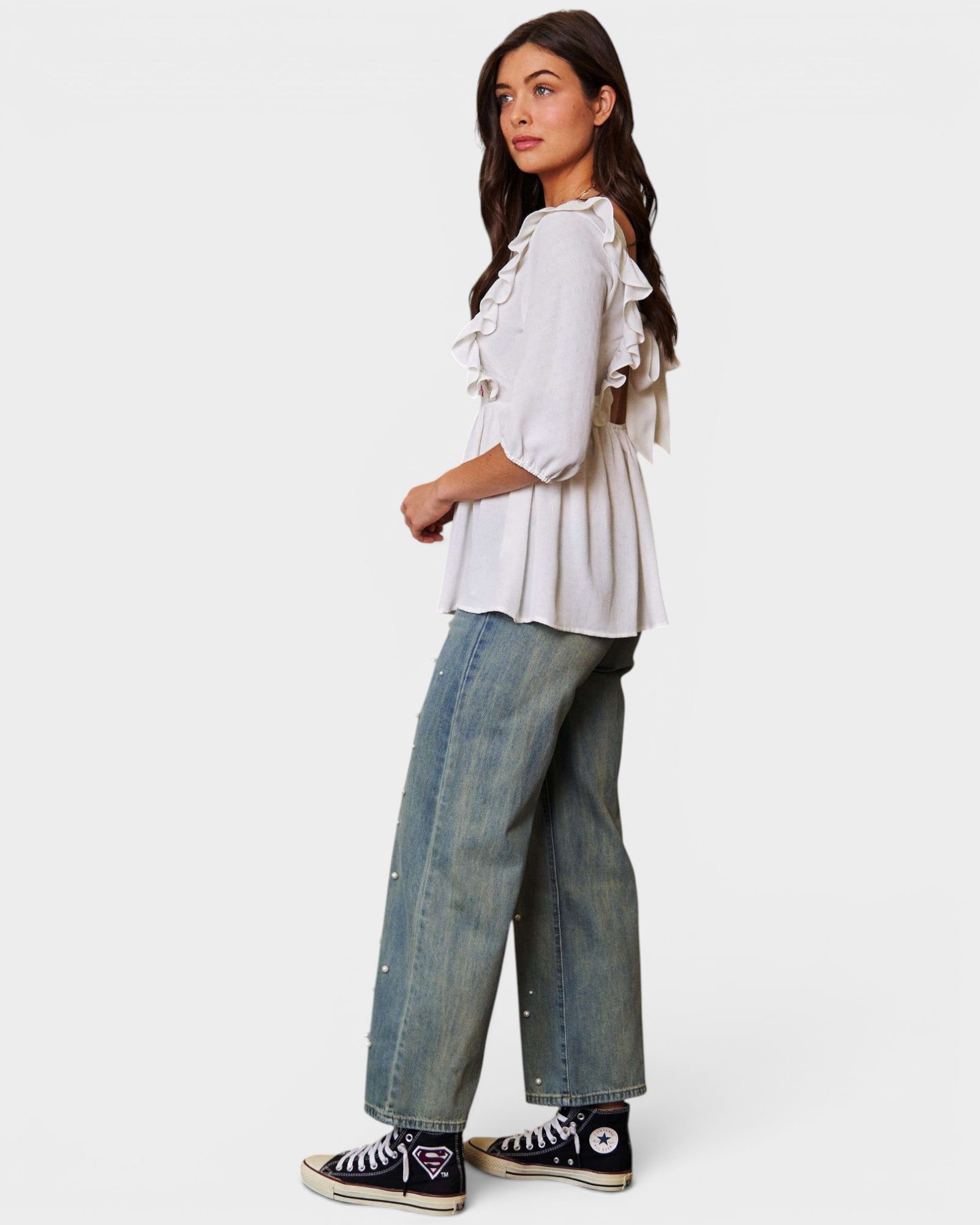 Woman wearing a white blouse with ruffles and blue jeans on a white background