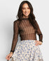 Woman wearing a sheer brown top and floral skirt on a plain background
