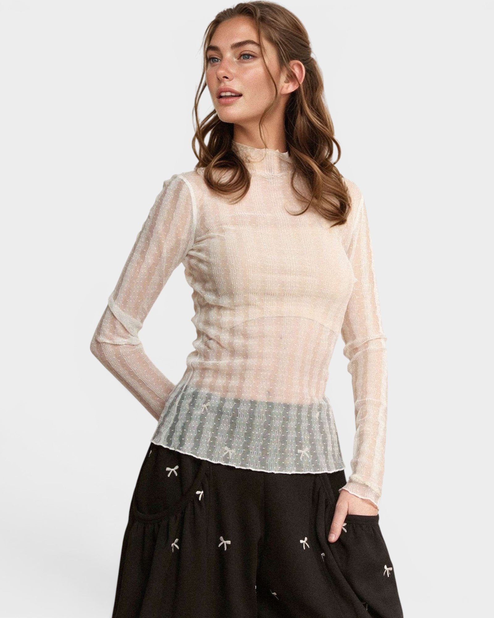 Woman wearing a beige sheer top over a patterned shirt with black pants on a white background