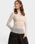 Woman wearing a beige sheer top over a patterned shirt with black pants on a white background