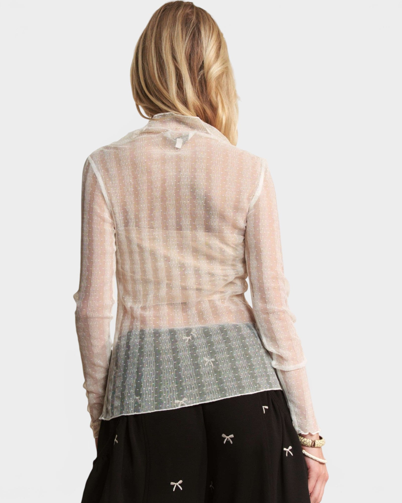 Woman wearing a sheer beige long-sleeve top over a patterned skirt on a white background