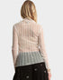 Woman wearing a sheer beige long-sleeve top over a patterned skirt on a white background