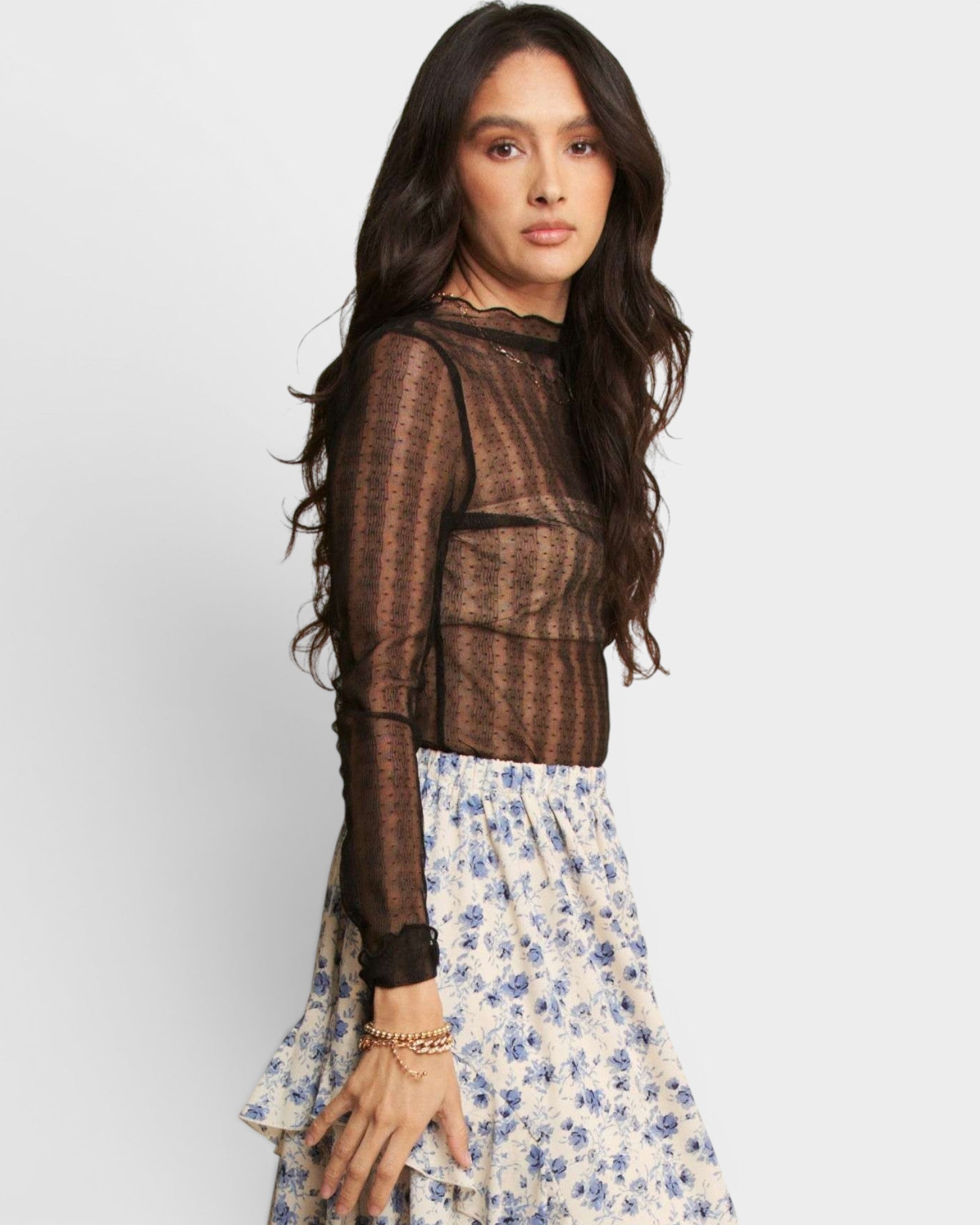 Woman wearing a sheer black top with a floral skirt on a white background