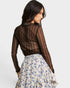 Woman wearing a sheer brown top and floral skirt on a plain background