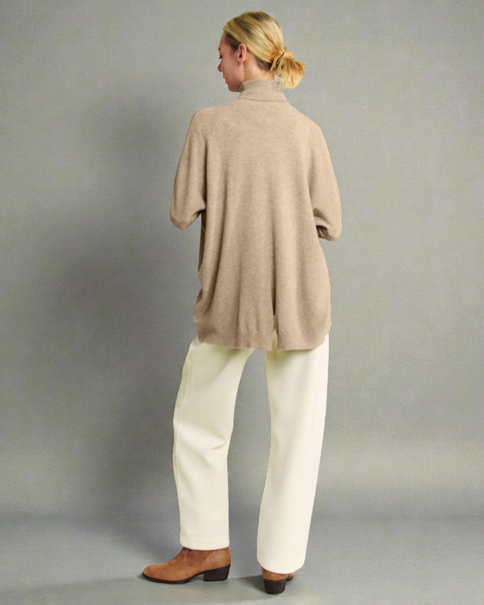 Person wearing a beige sweater and white pants against a gray background