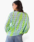 A woman shown from the back wearing a light blue knit sweater with bright lime green vertical stripes and small brown and black heart-shaped cutouts, paired with blue jeans against a plain white background.
