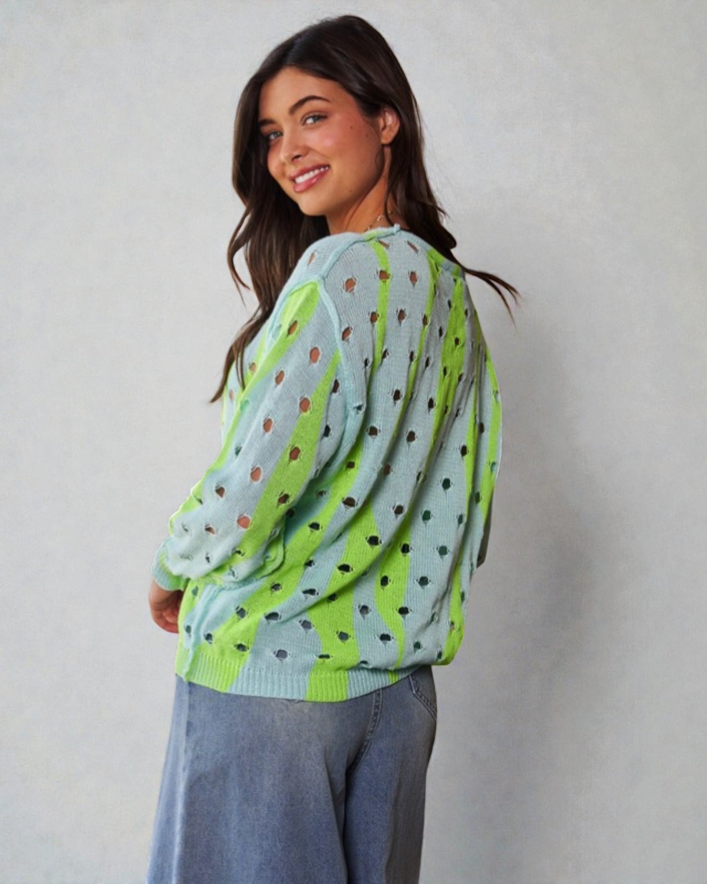 Woman wearing a light blue sweater with green accents and black polka dots, standing against a plain background.