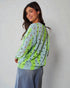 Woman wearing a light blue sweater with green accents and black polka dots, standing against a plain background.