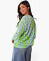 A woman wearing a light blue and lime green knit sweater with a black and brown polka dot pattern, paired with blue jeans, photographed against a plain white background.