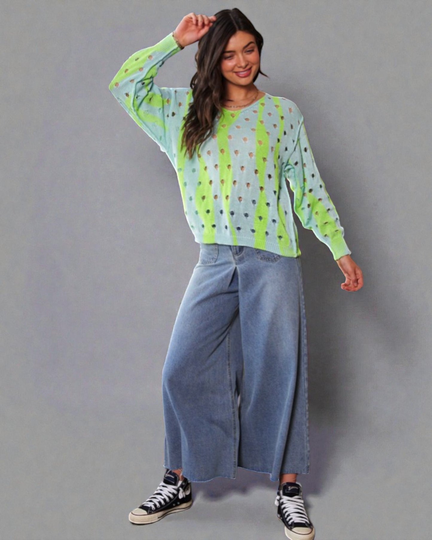 Woman wearing a green and blue patterned top with wide-leg jeans on a gray background