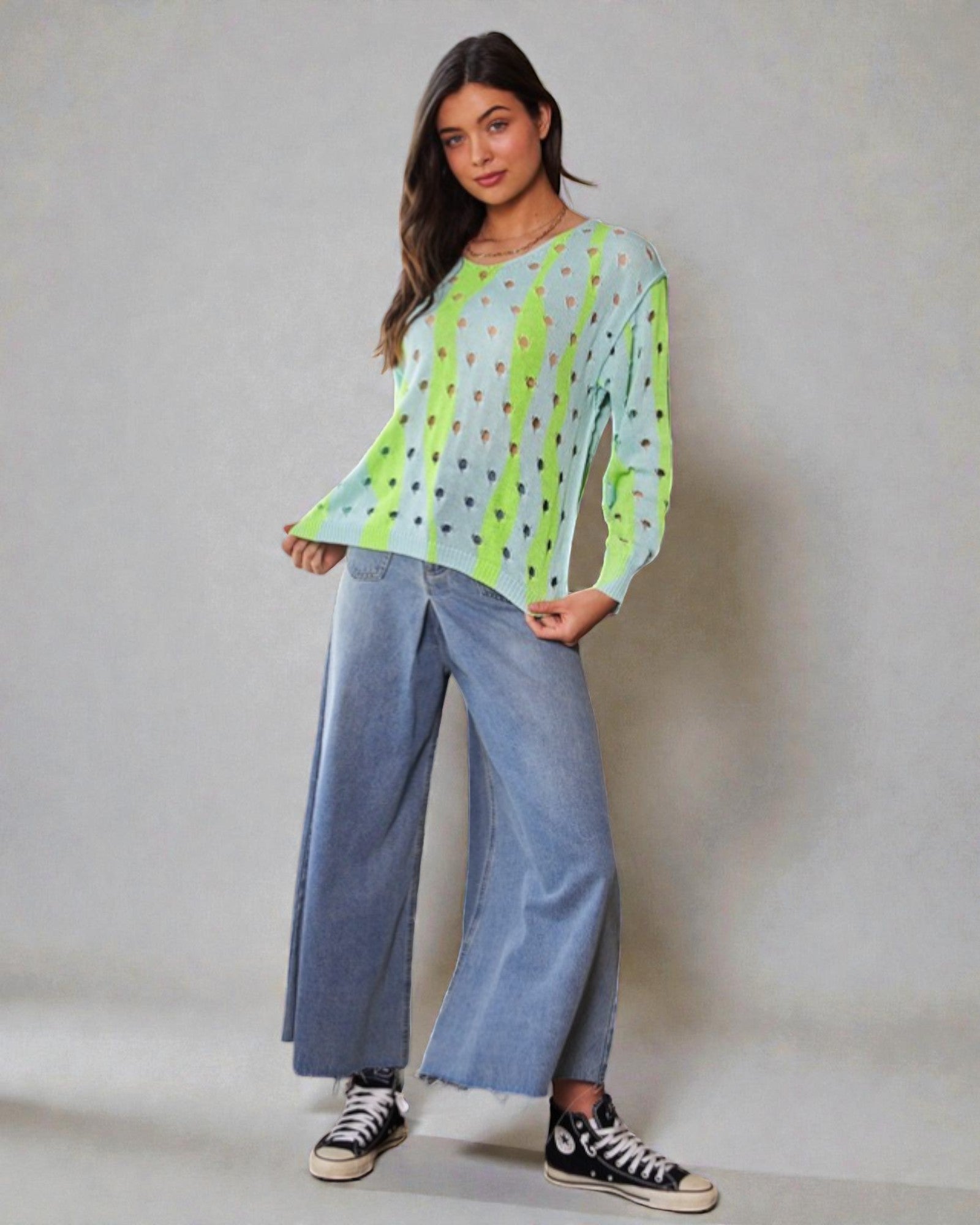 Woman wearing a light green patterned top and blue jeans against a plain background