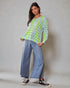 Woman wearing a light green patterned top and blue jeans against a plain background