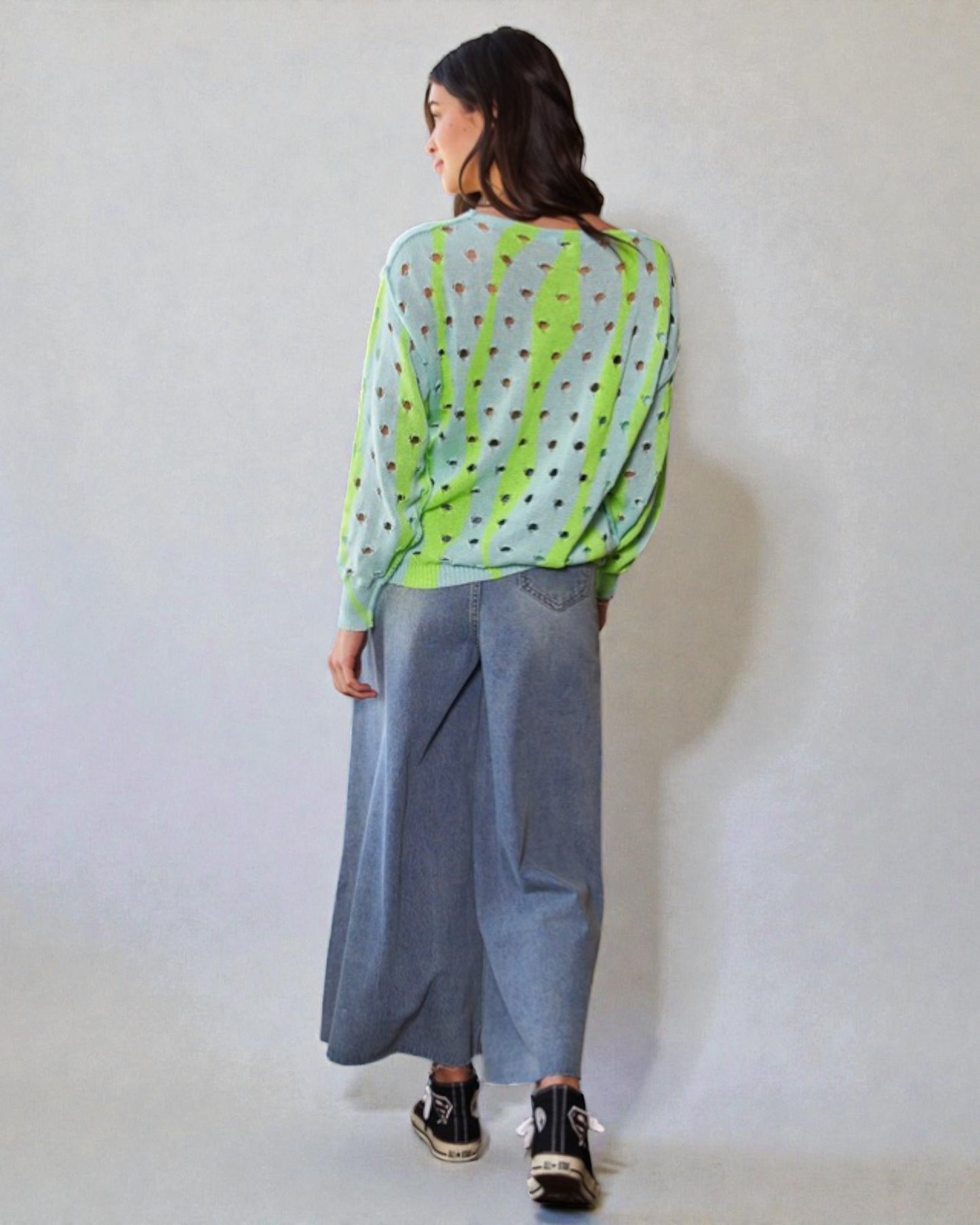 Person wearing a green and white patterned top with gray pants on a plain background