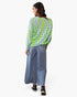 A woman is shown from behind wearing a sheer light blue-green long-sleeve top with vertical neon green stripes and black polka dots, paired with wide-leg blue jeans and black sneakers, against a plain white background.
