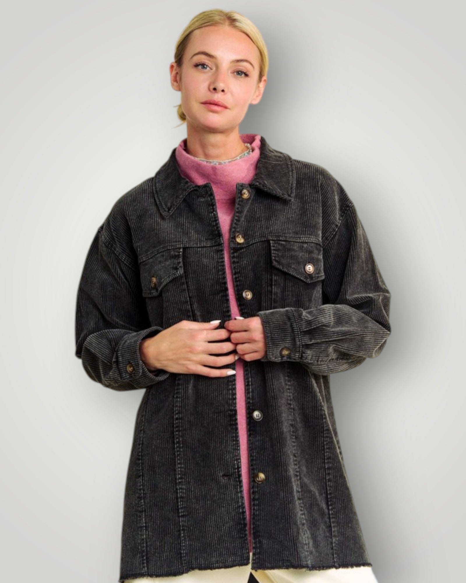 Person wearing a dark denim jacket over a pink sweater on a plain background