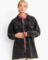 A woman wearing an oversized dark charcoal corduroy jacket over a pink mock-neck top, photographed against a clean white studio background.