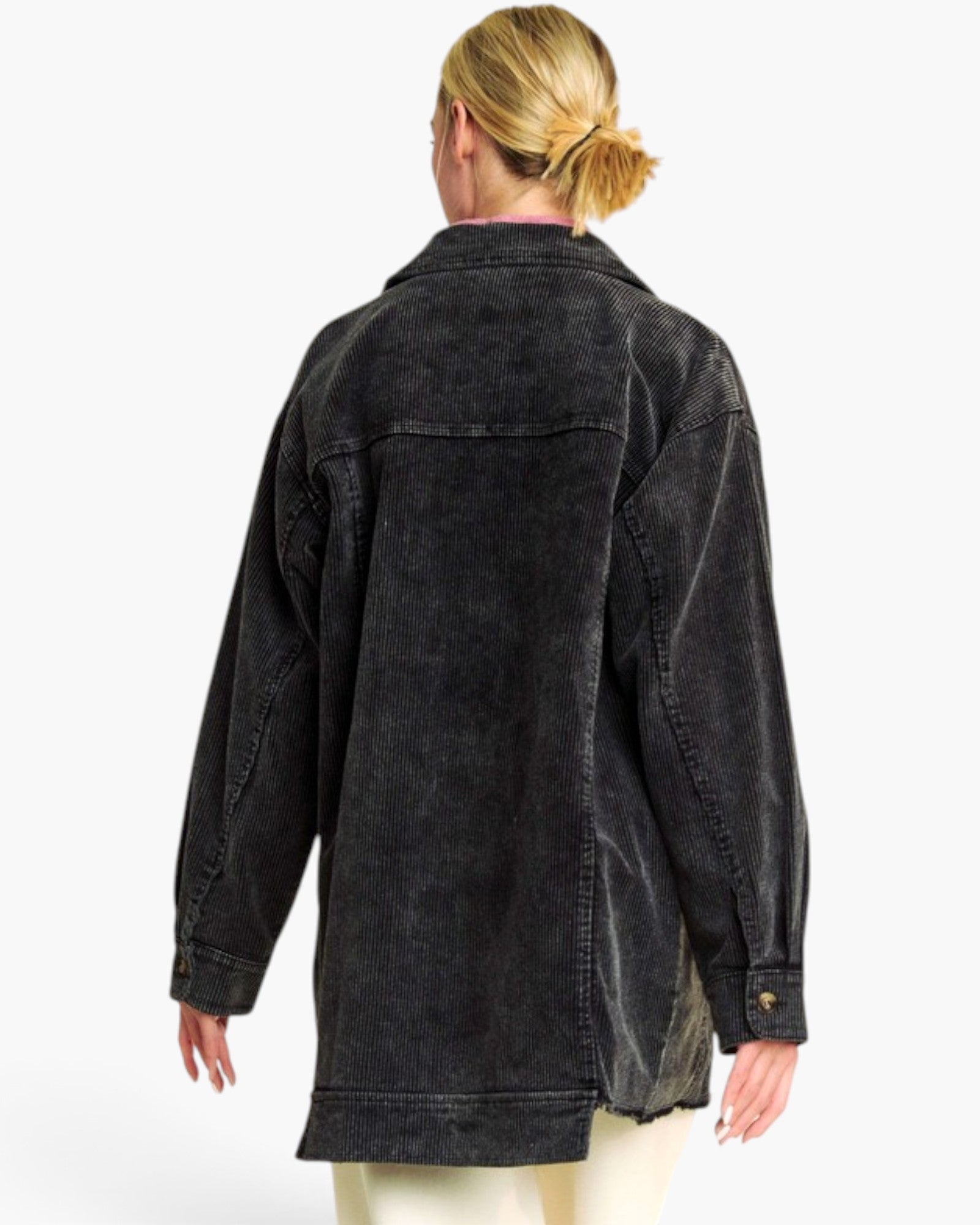 A woman viewed from the back wearing an oversized dark washed denim jacket over a pink top and cream pants, set against a plain white studio background.