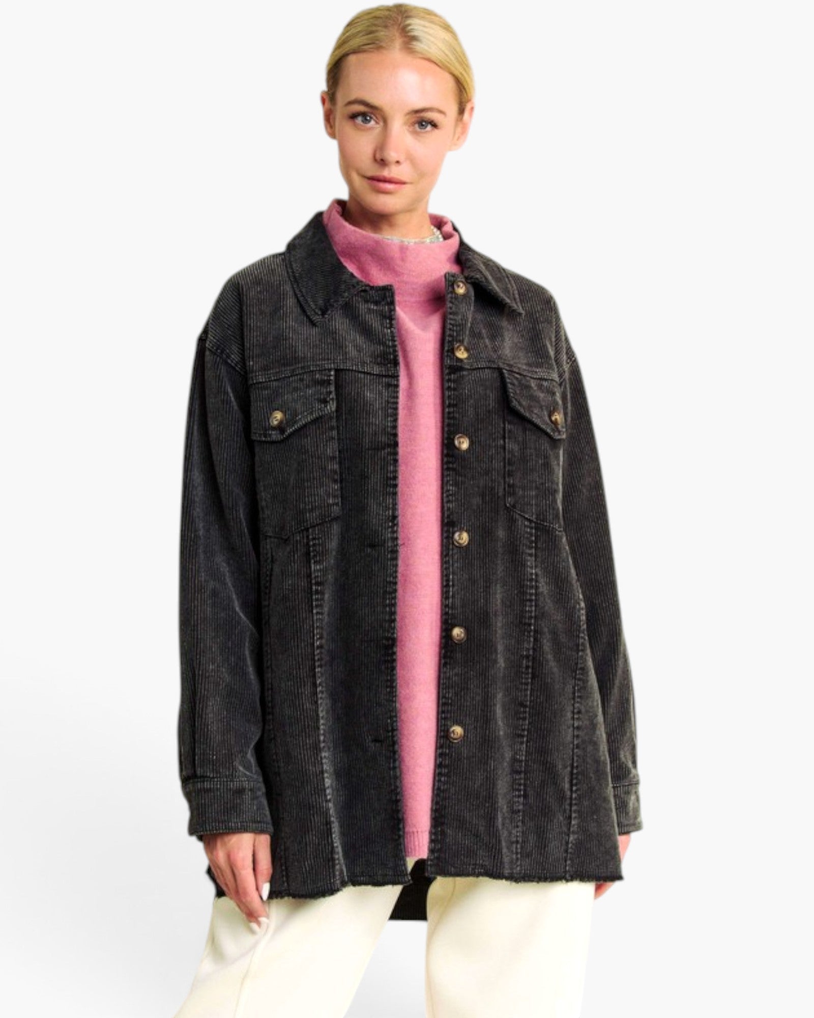 A woman modeling an oversized black washed denim jacket over a pink turtleneck sweater and cream pants, photographed against a clean white studio background.
