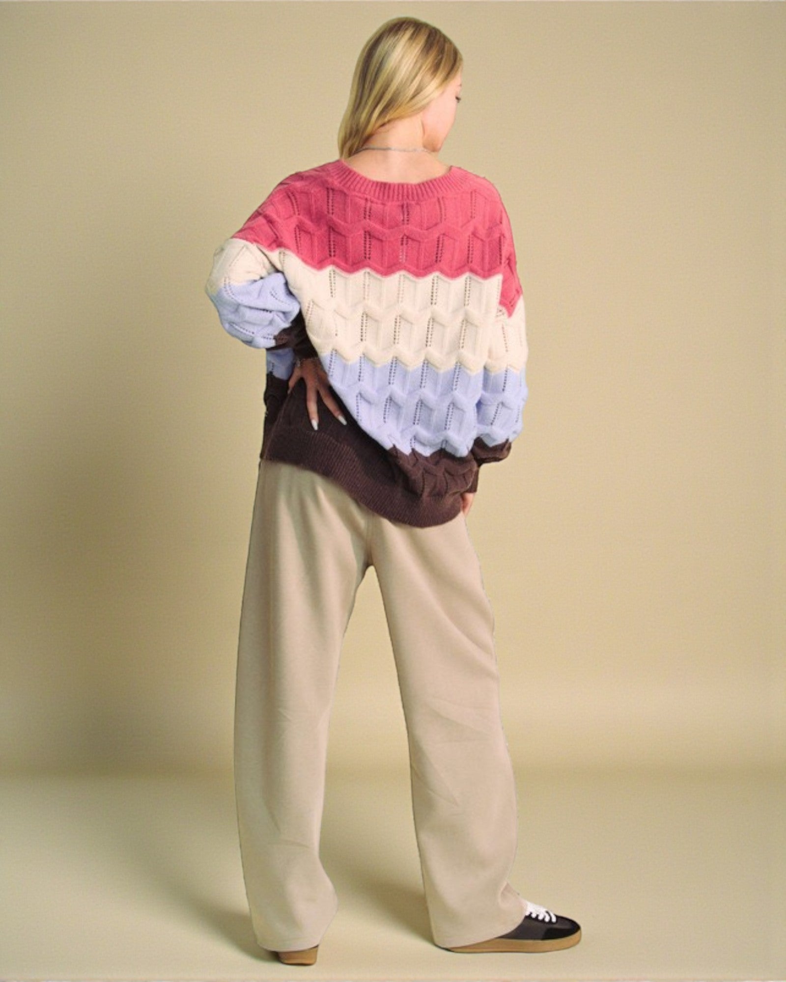 Person wearing a colorful sweater and beige pants on a plain background