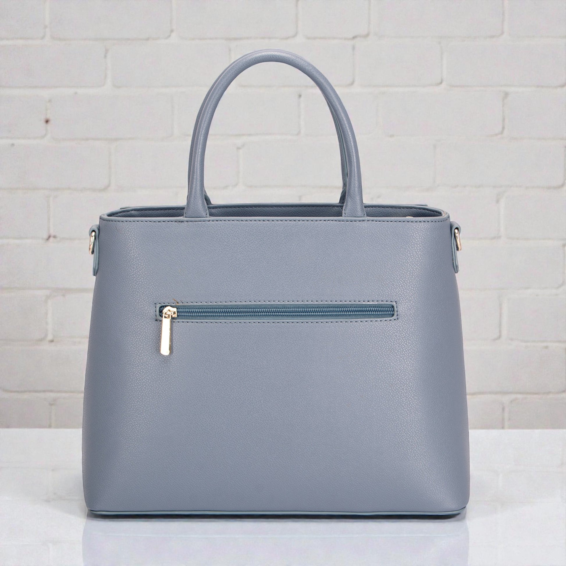 Gray handbag with a gold zipper on a white surface and light gray brick wall background