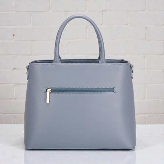 Gray handbag with a gold zipper on a white surface and light gray brick wall background
