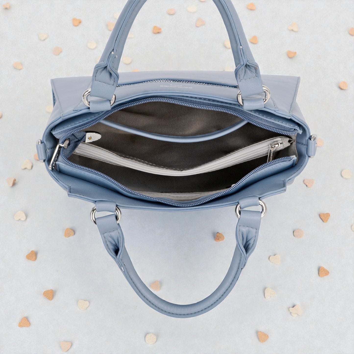 Blue handbag with open front compartment on a light gray background with heart shapes.