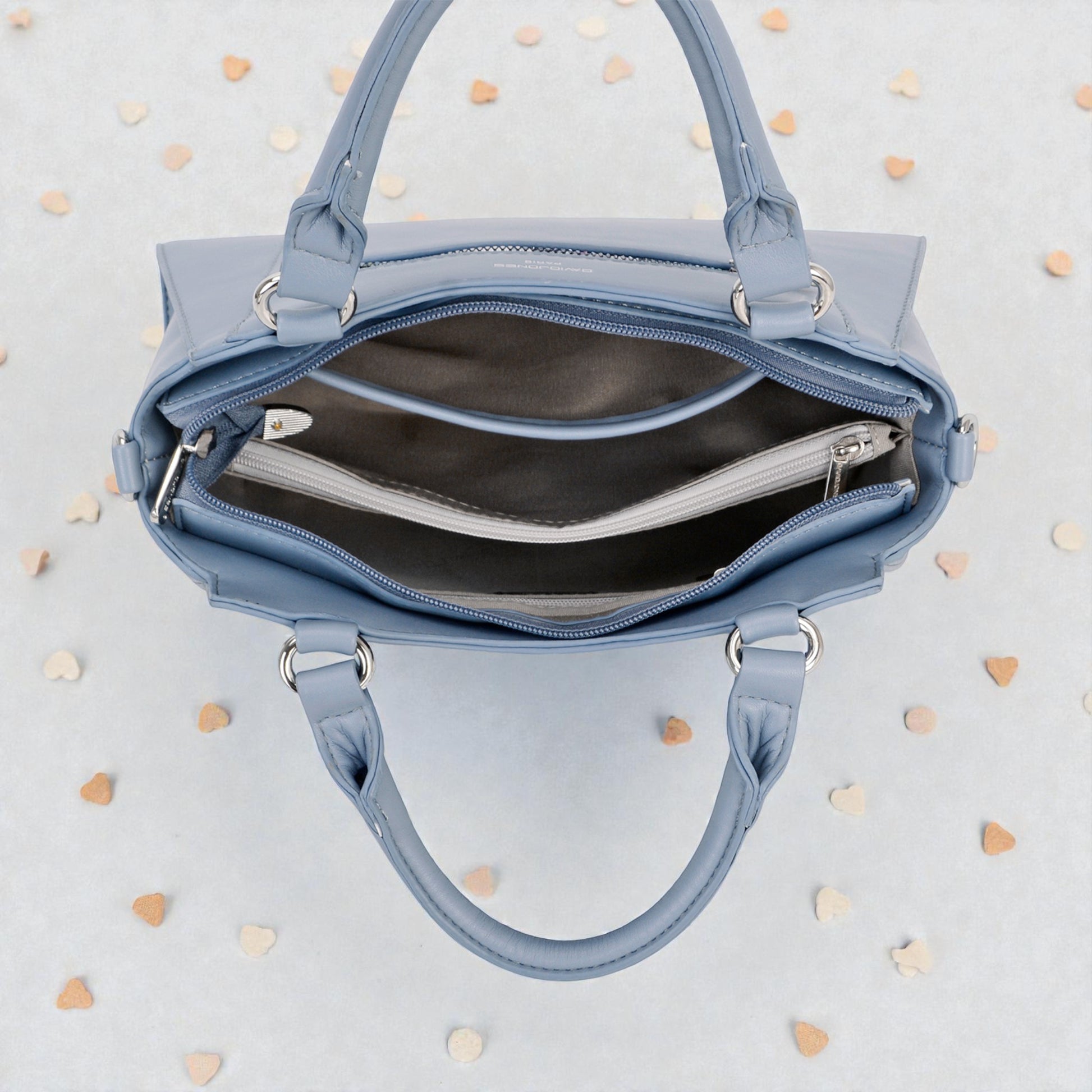 Blue handbag with open front compartment on a light gray background with heart shapes.