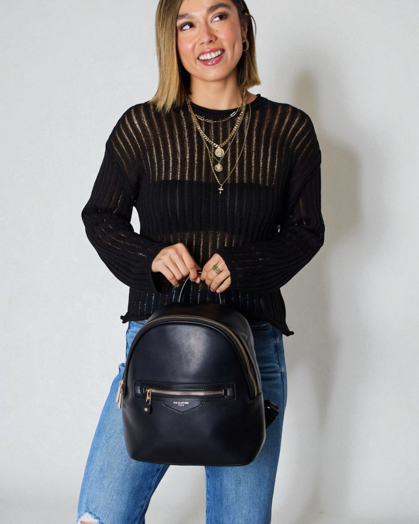 Woman holding a black backpack against a plain background