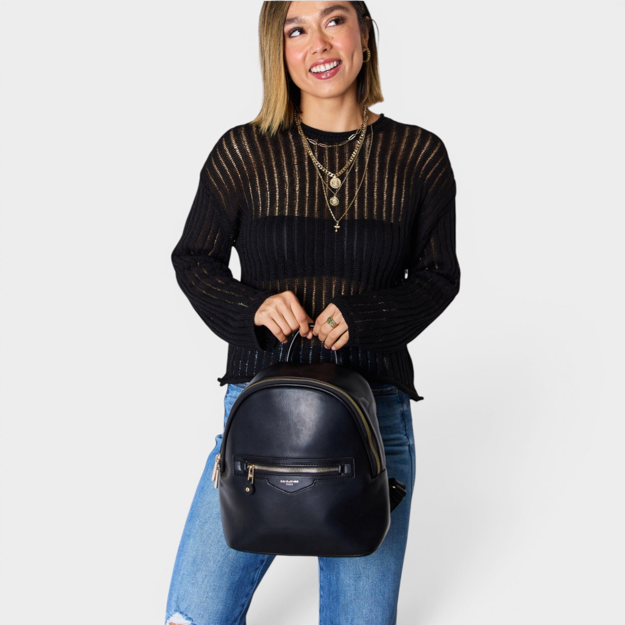 Woman holding a black backpack against a plain background