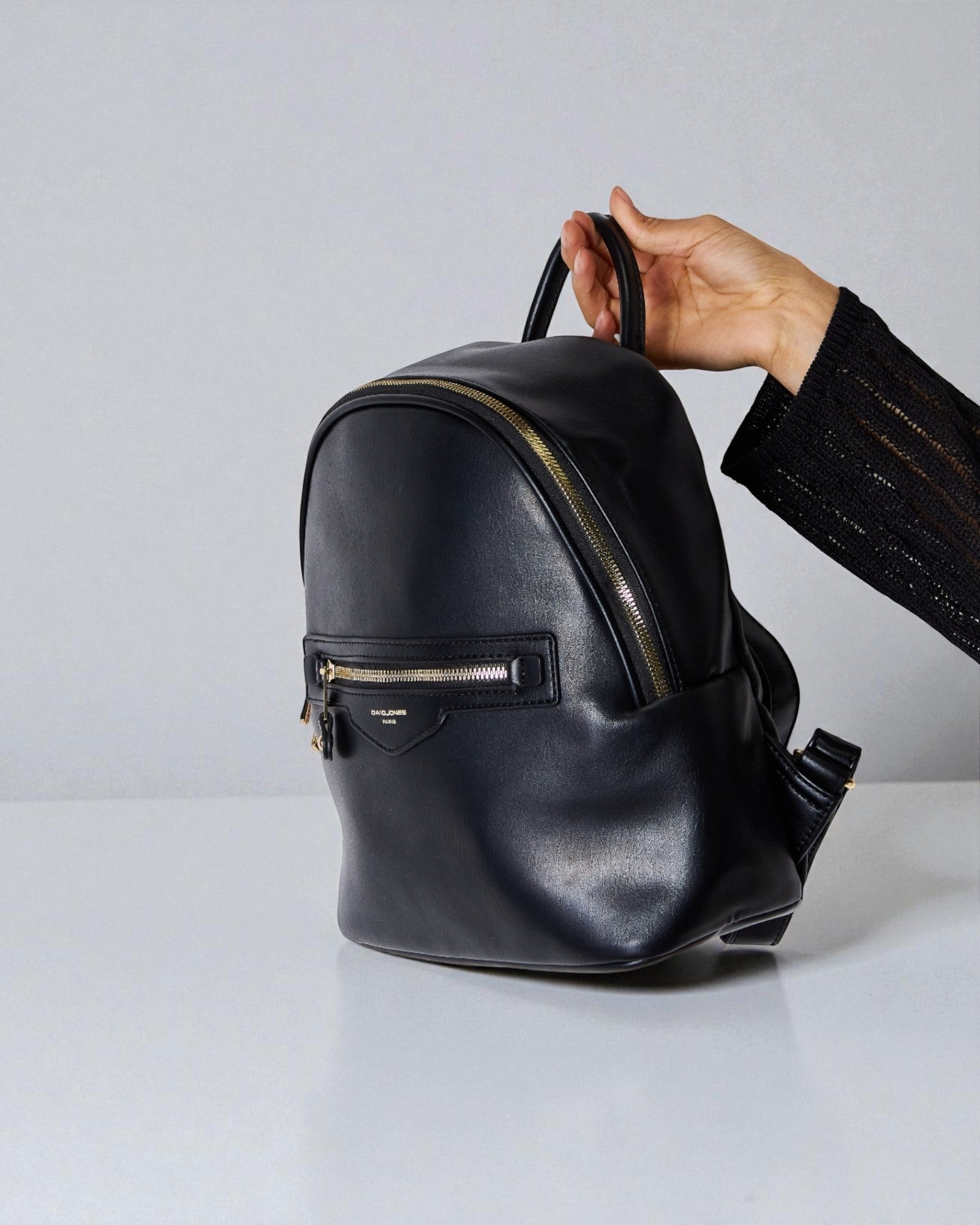 Black leather backpack held by a hand against a light gray background