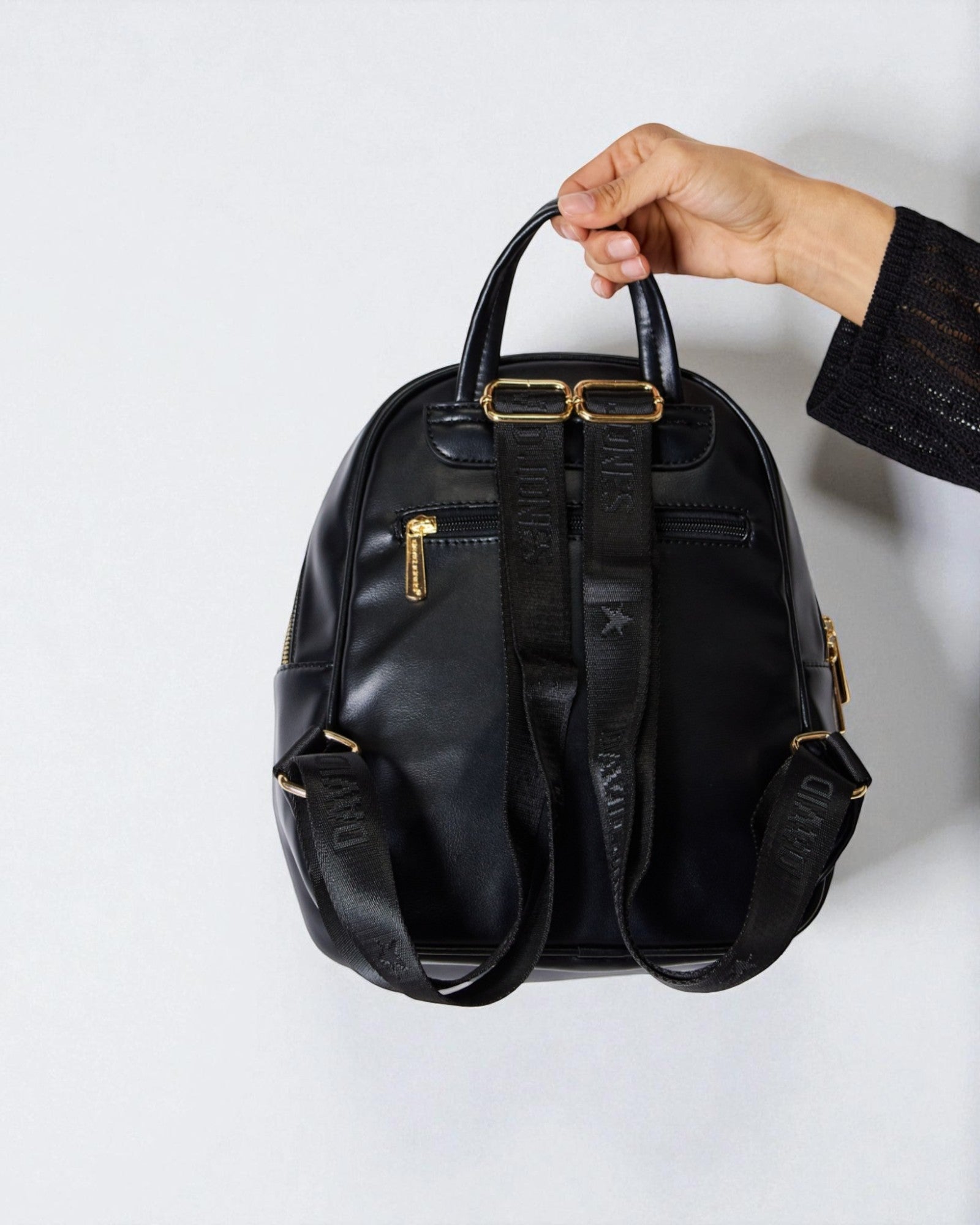 Black backpack held by a hand on a white background