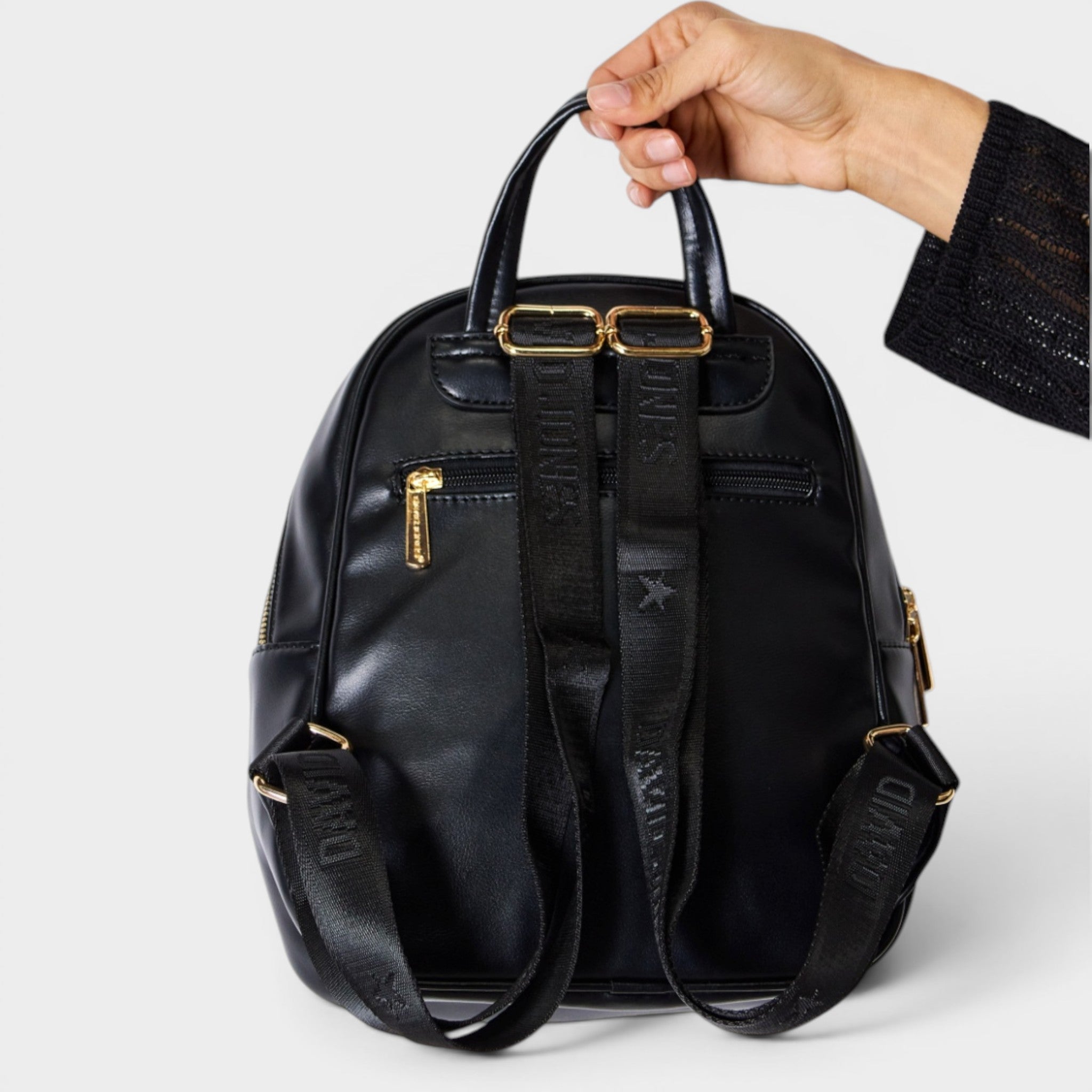 Black backpack held by a hand on a light gray background