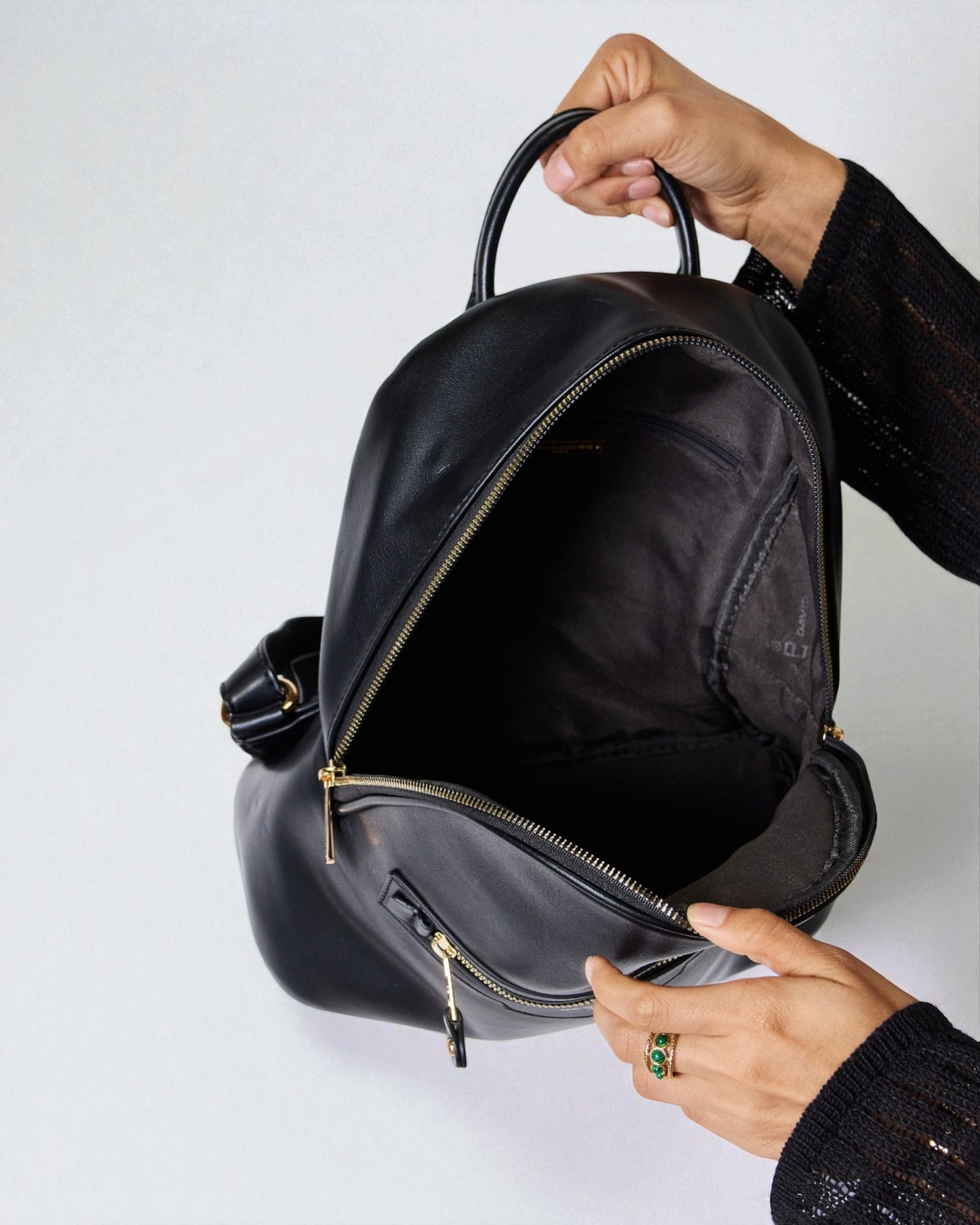 Person holding a black backpack with a plain background