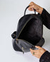 Person holding a black backpack with a plain background