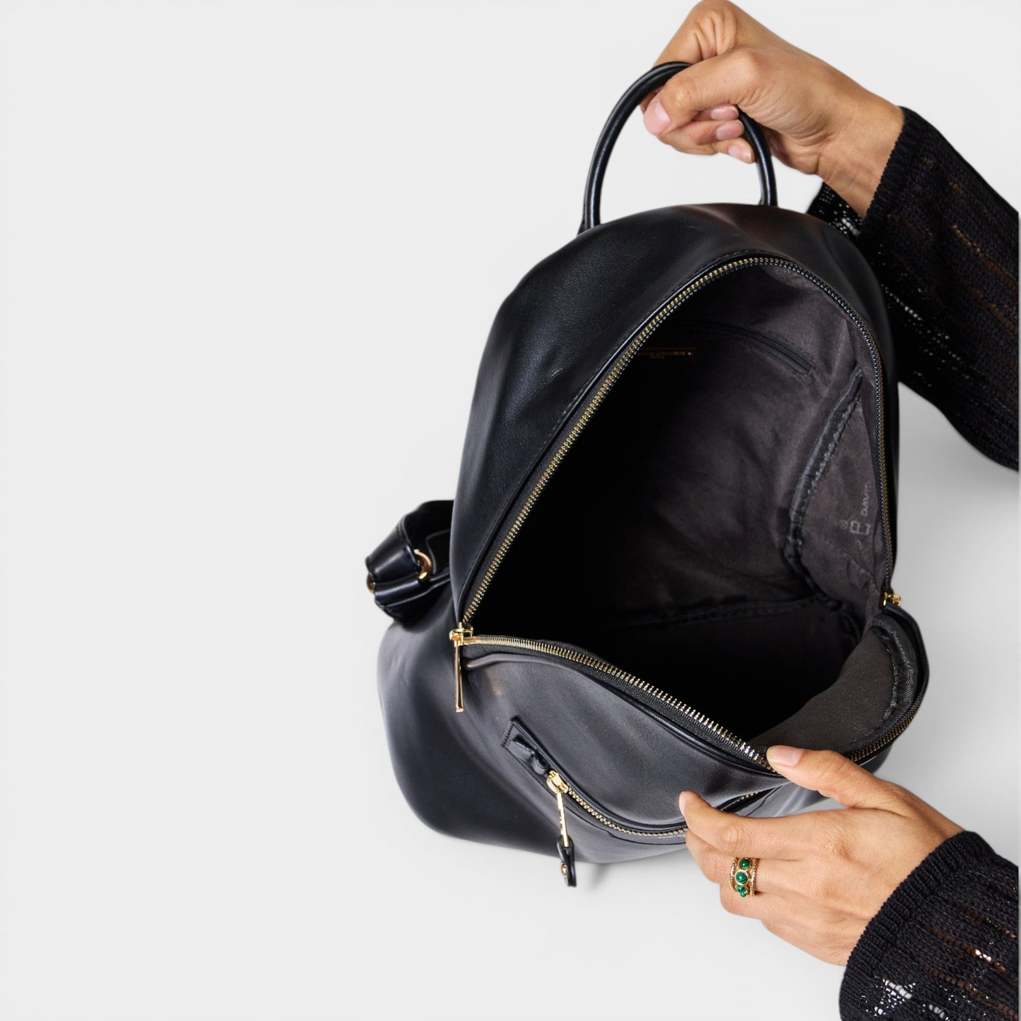 Black backpack being held open by a hand on a light gray background