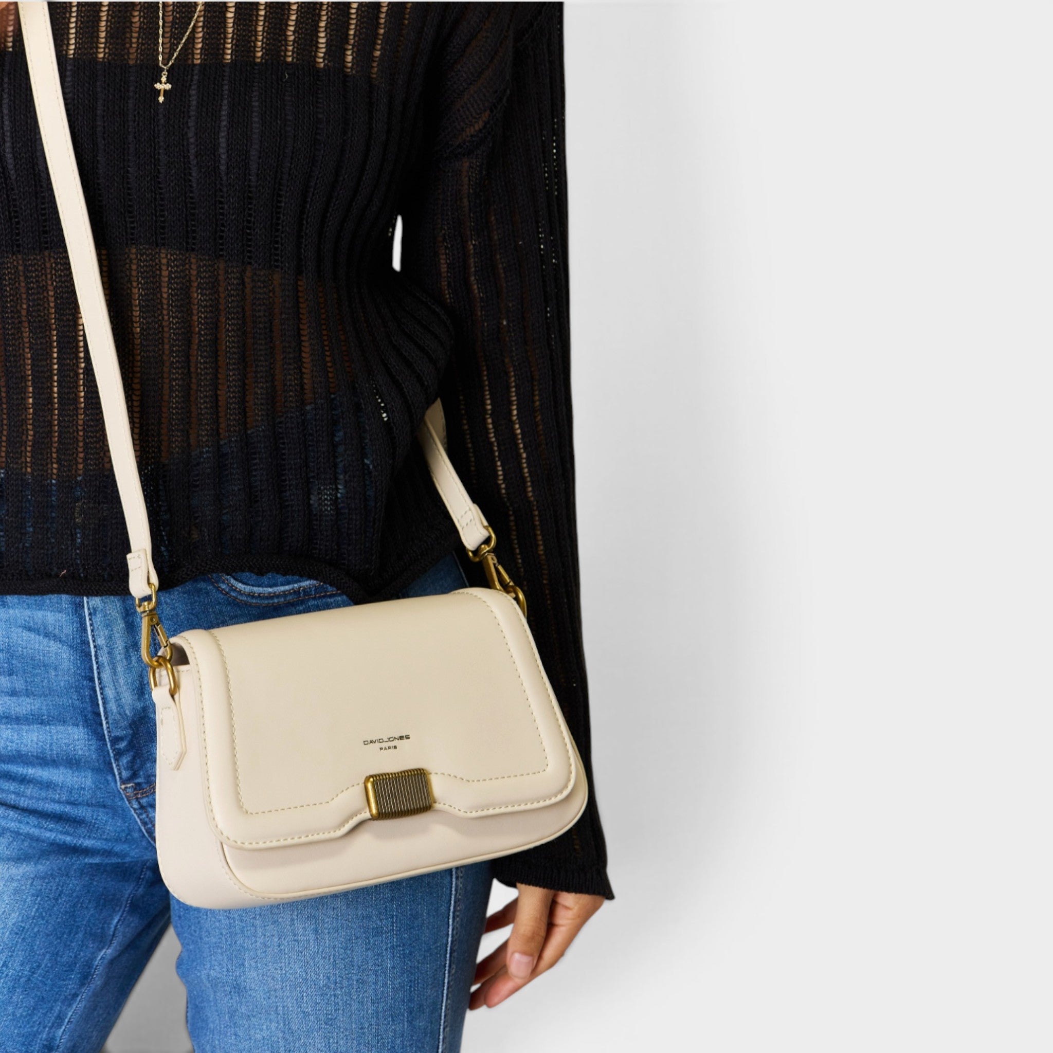 Beige handbag with gold clasp held by a person wearing a black sweater and blue jeans on a white background