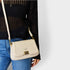 Beige handbag with gold clasp held by a person wearing a black sweater and blue jeans on a white background