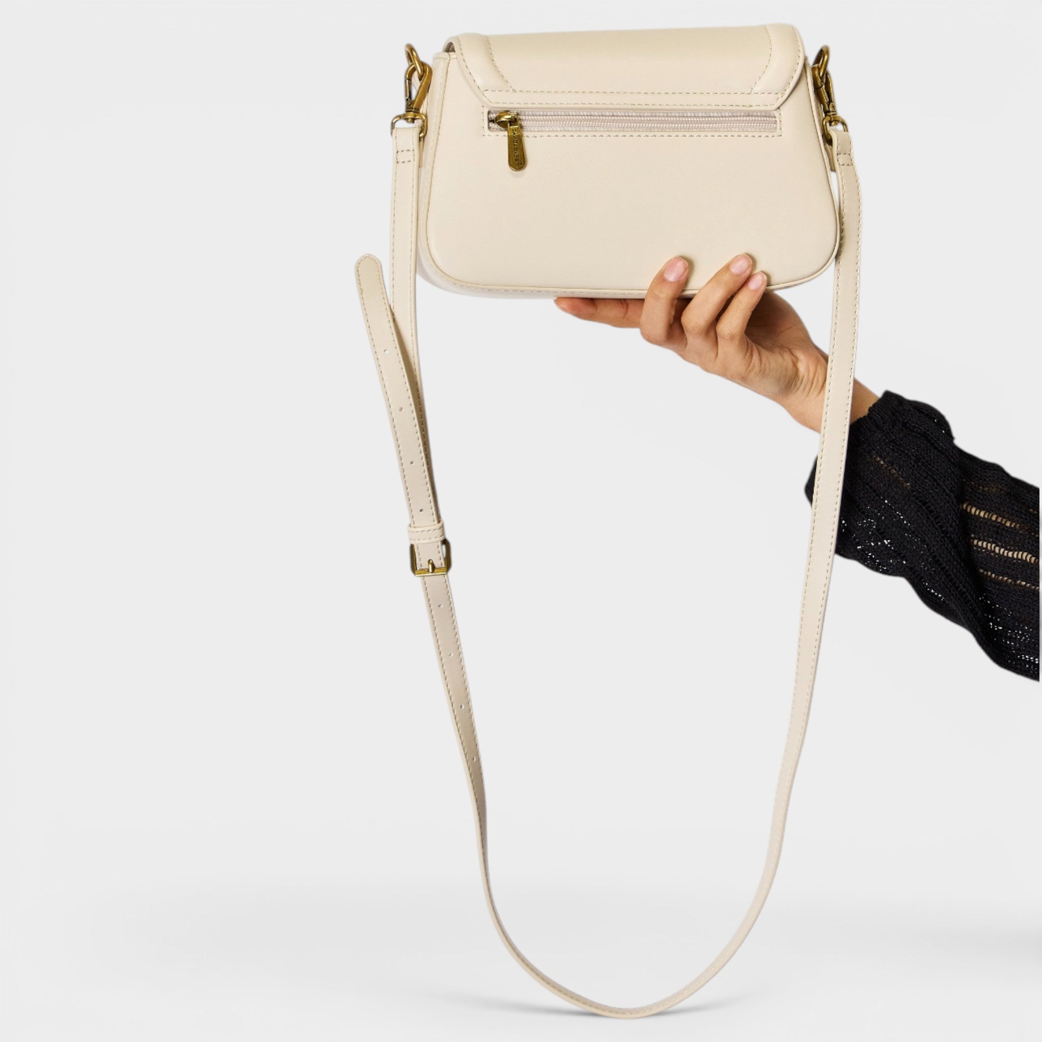 Beige handbag with a strap held by a hand on a light gray background