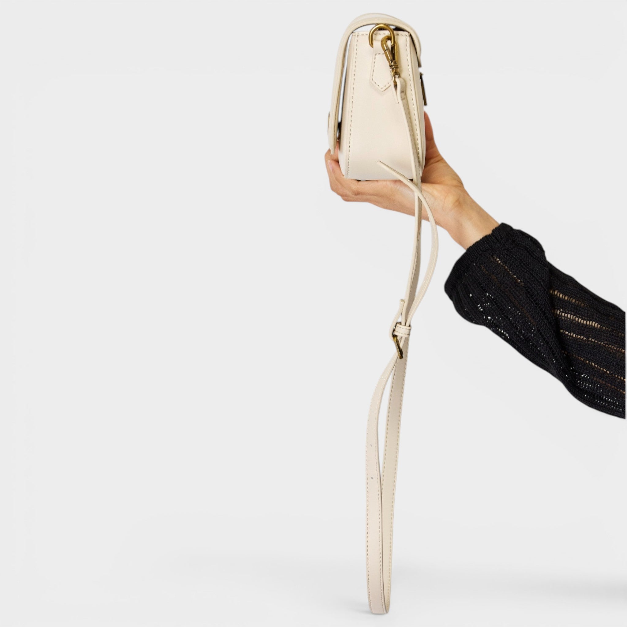 Hand holding a beige handbag with a strap against a light gray background