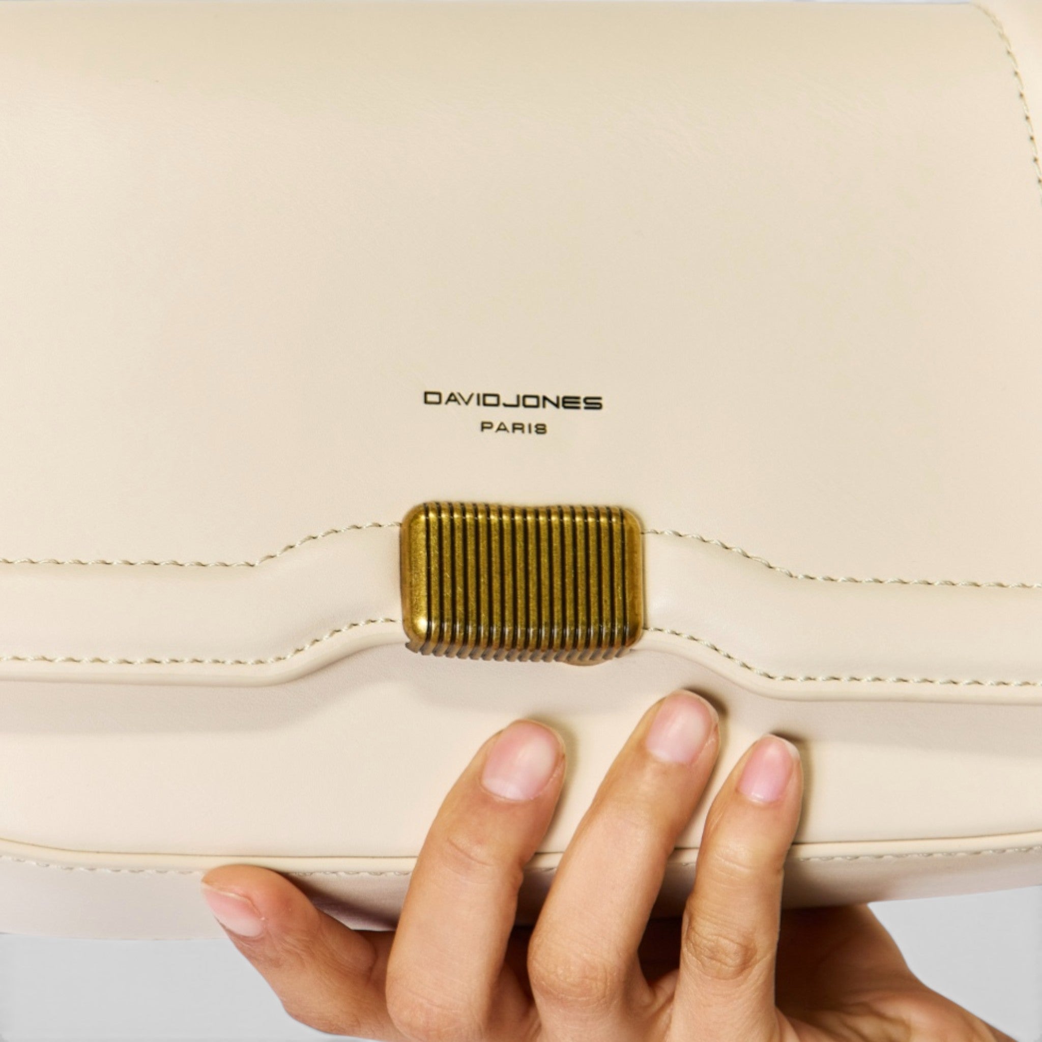 Beige handbag with gold clasp held by a hand, brand 'DAVIDJONES PARIS' visible.