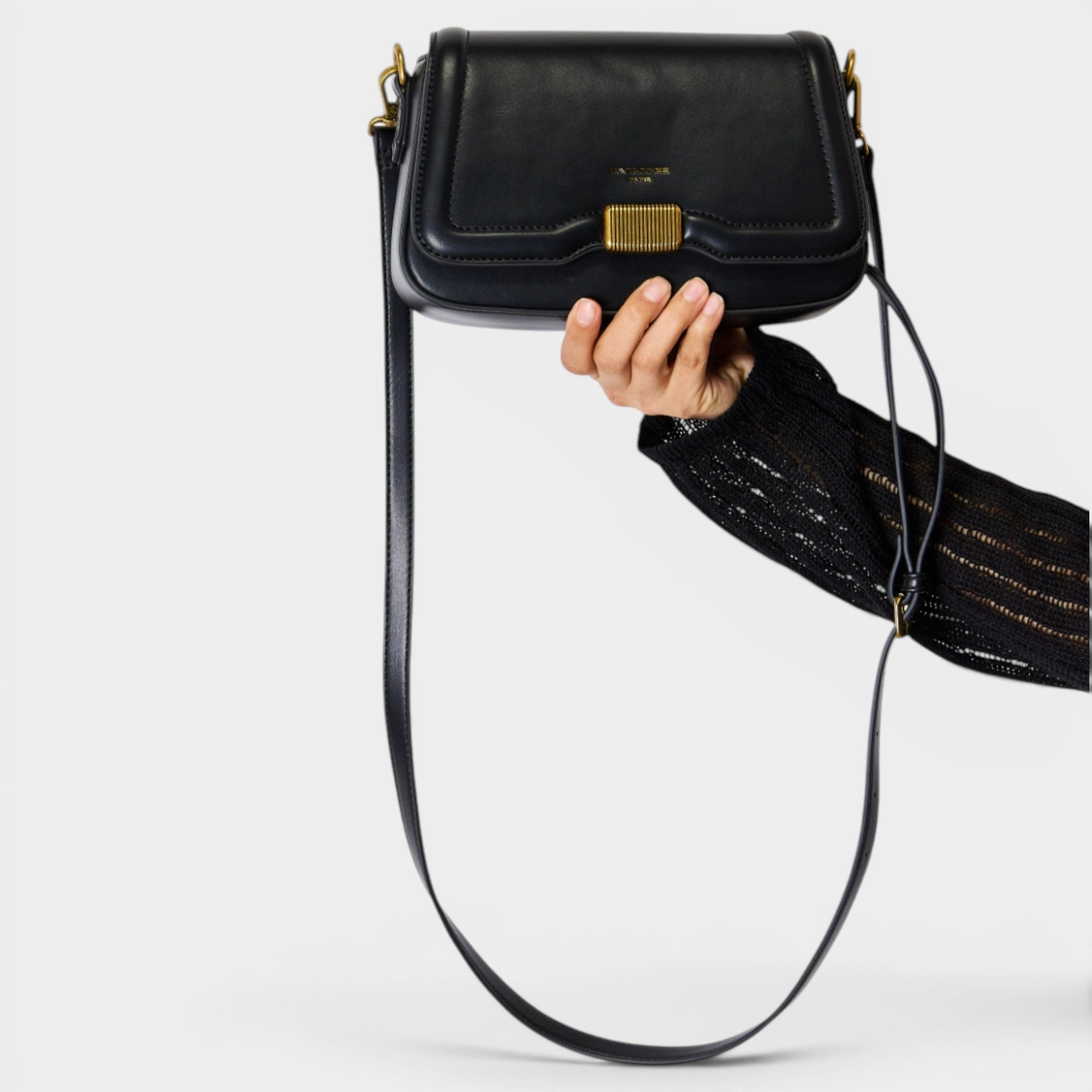 Black handbag with a gold clasp held by a hand on a light gray background